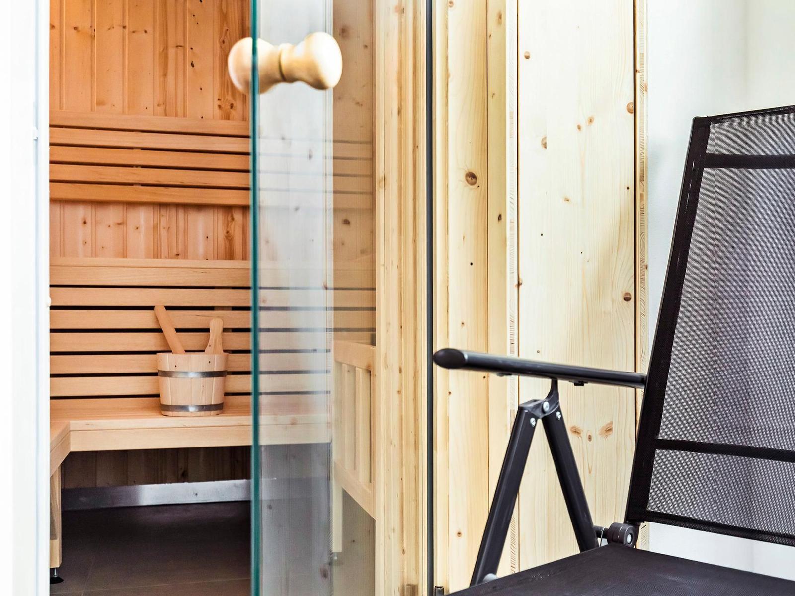 Sauna mit Holzbank und Eimer. Außenseite mit Glas und Stuhl.