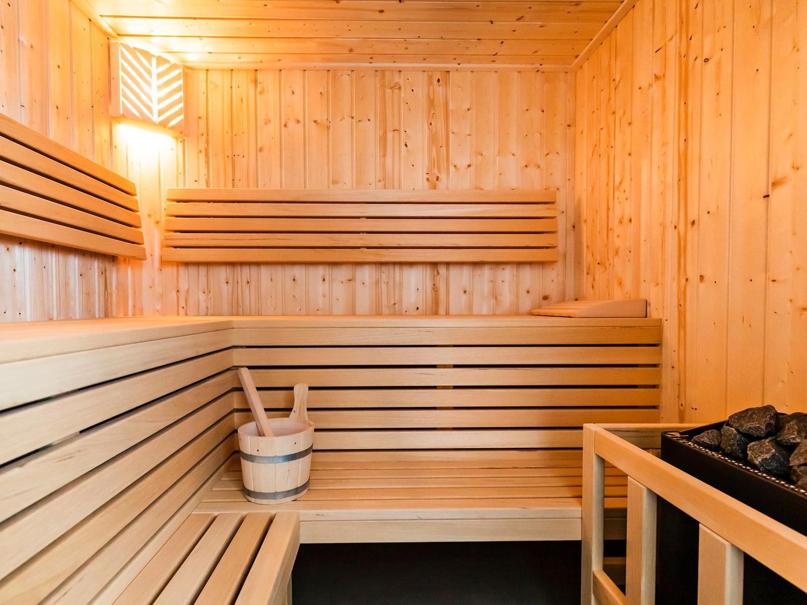 Sauna mit Holzbanken und Holzwand. Holzschale mit Besen. Steinmulde mit Steinen.