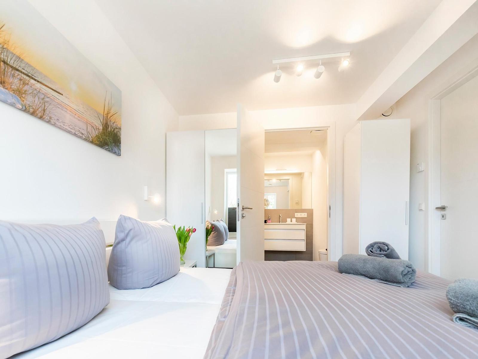 Schlafzimmer mit Bett, Wandbild und Blick in das Bad.