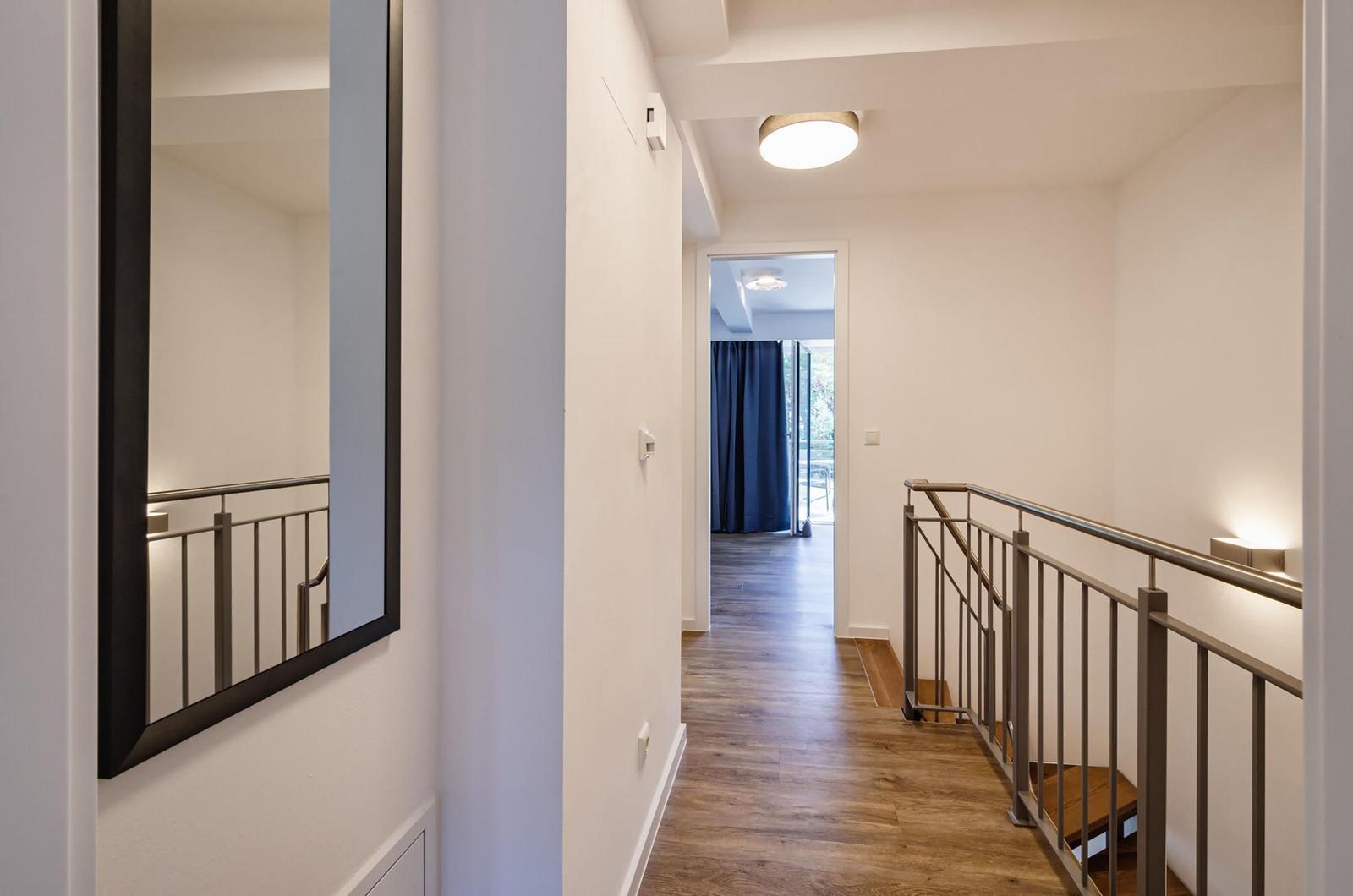 Flur mit Holzboden, Spiegel und Geländer zur Treppe.
