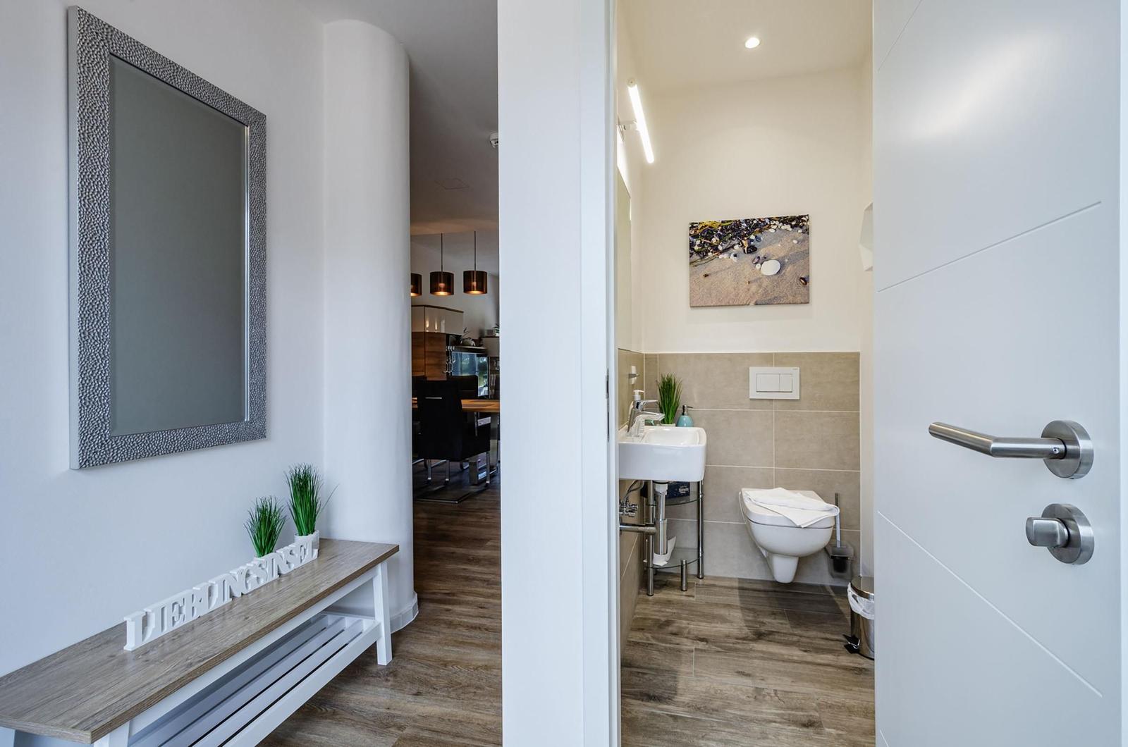 Flur mit Spiegel und Bank, Blick in Badezimmer mit Toilette und Waschbecken.
