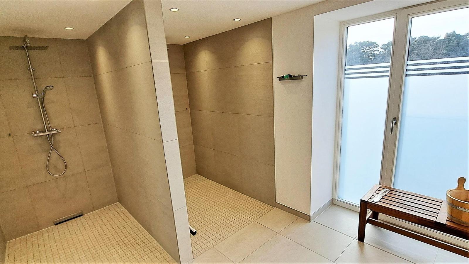 Dusche mit Duschbrause und Holzbank vor Fenster