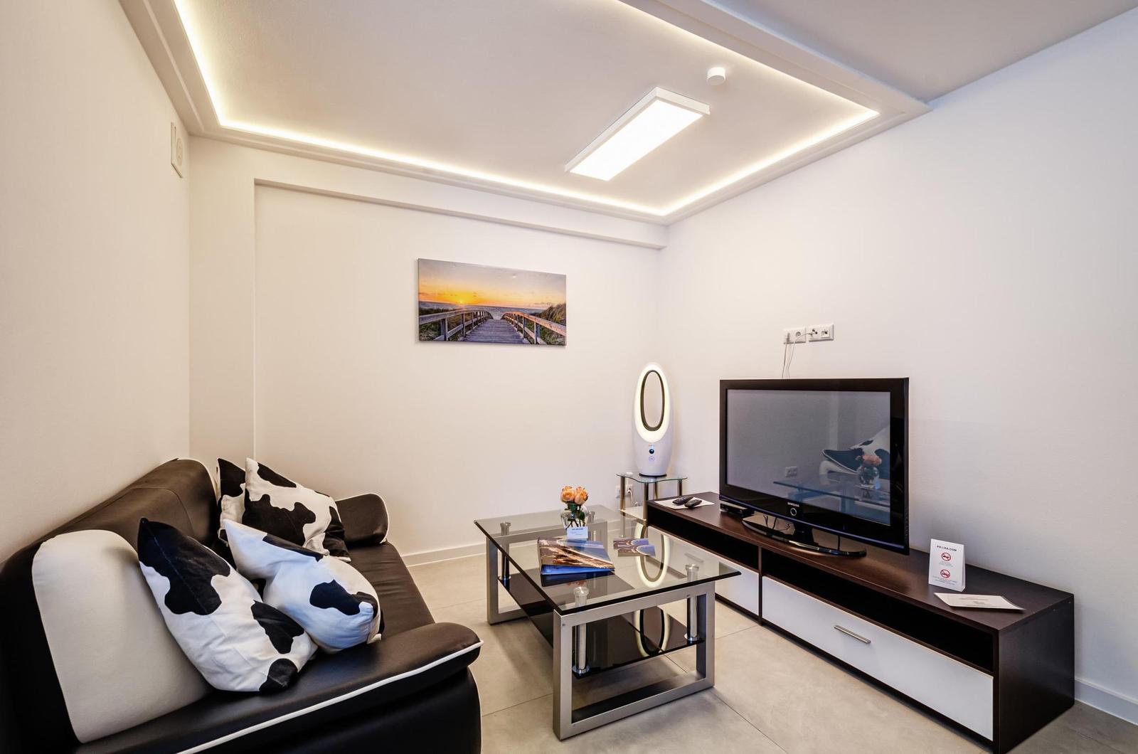 Wohnzimmer mit Sofa, Fernseher und Glas-Tisch