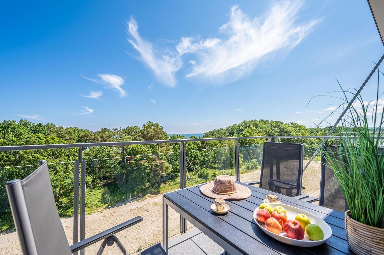 Terrasse mit Tisch, Stühlen und Obst. Blick auf Wald und Meer.