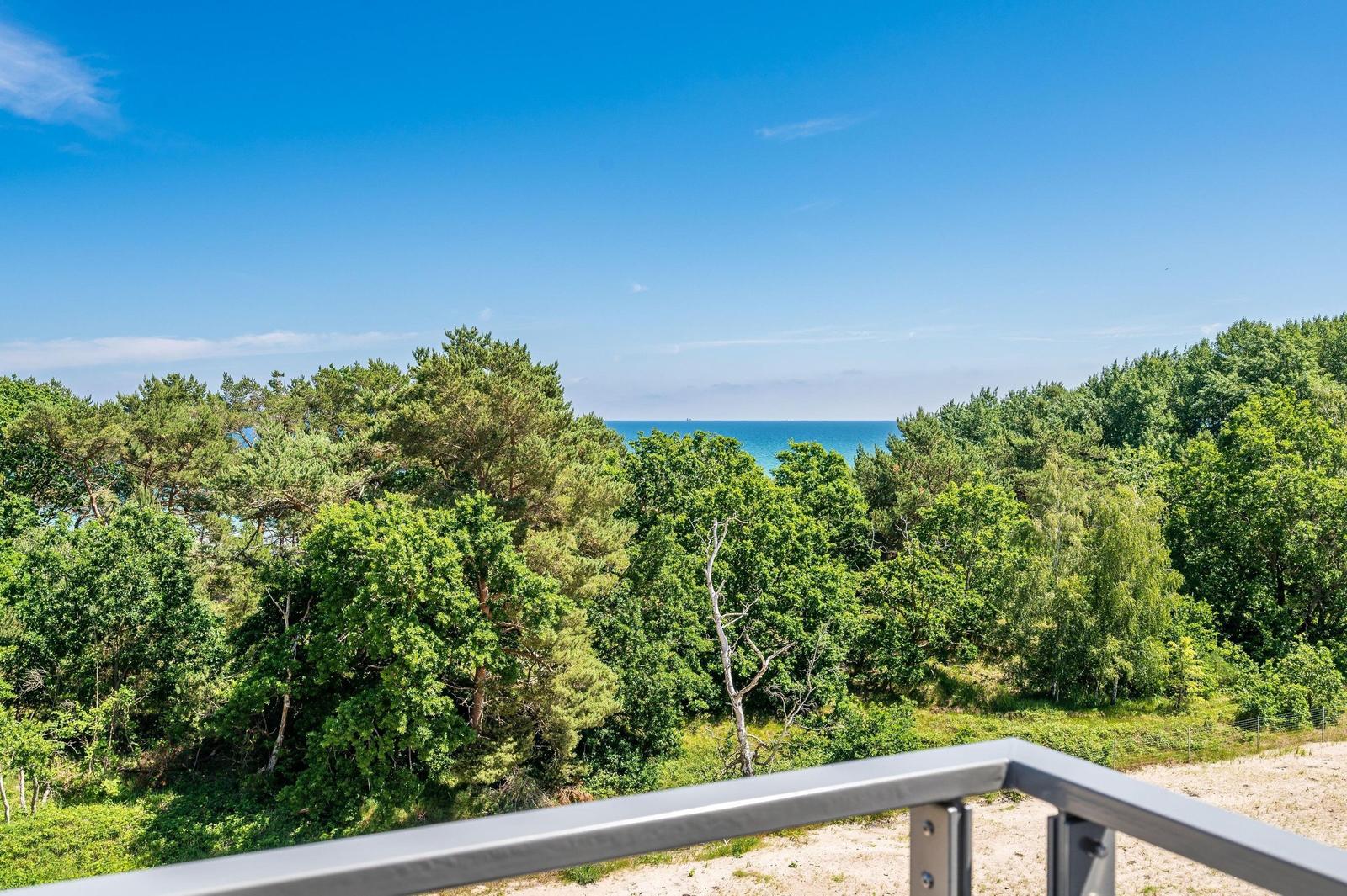 Blick von Balkon auf Wald und Meer unter blauem Himmel