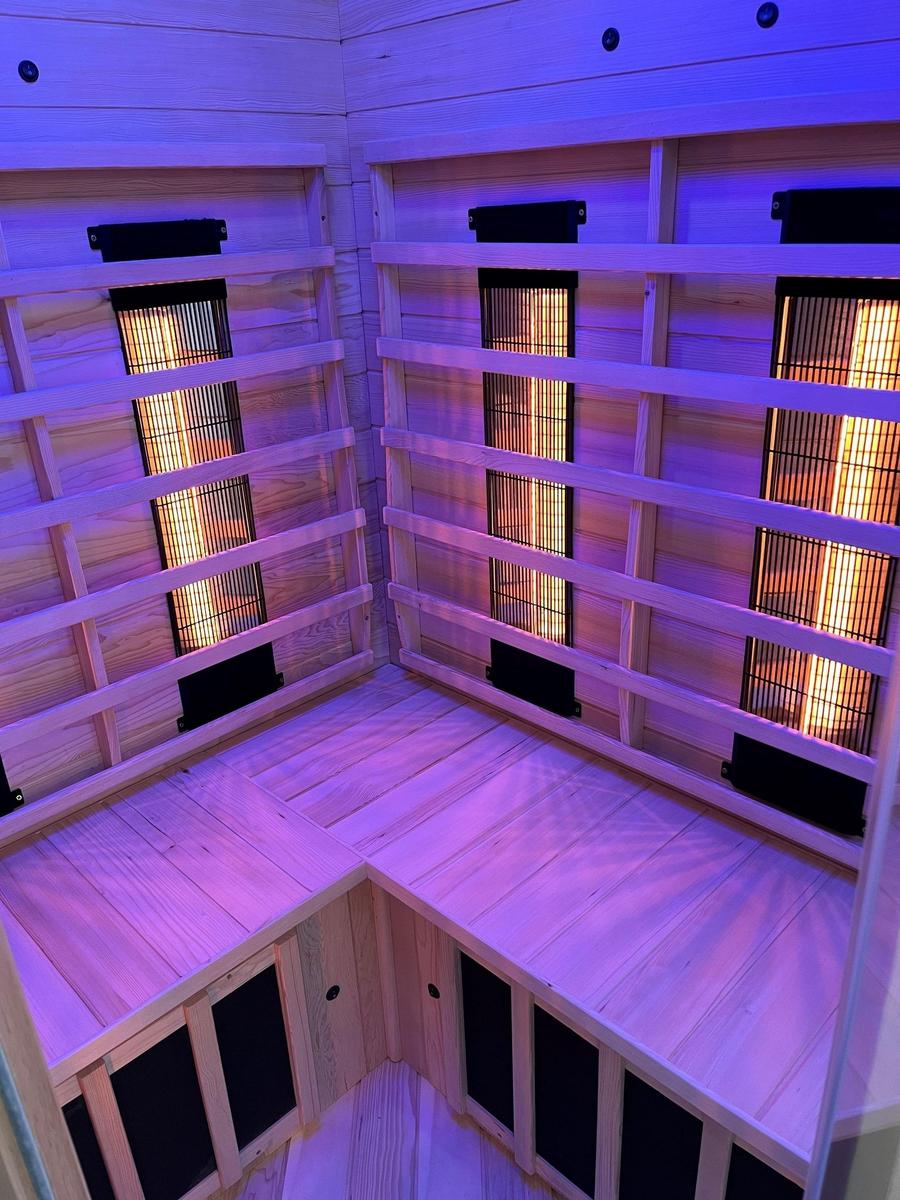 Sauna mit Holzwand und Heizungselementen, beleuchtet mit lila Licht.