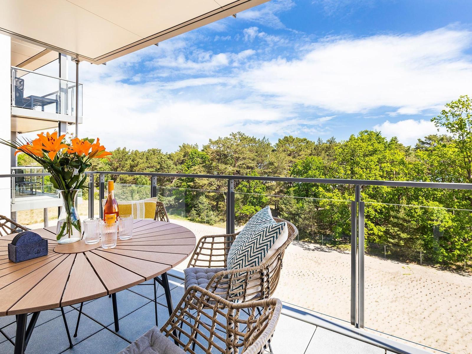 Terrasse mit Tisch, Stühlen und Blick auf Wald und Strand.