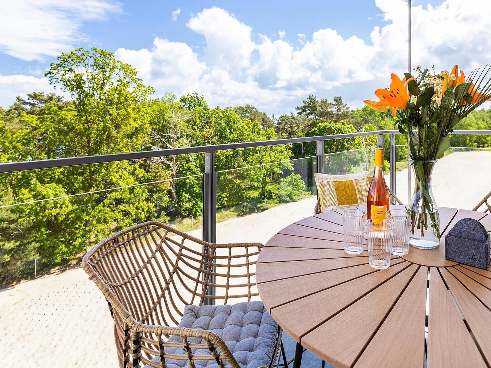 Terrasse mit Tisch, Stühlen und Blick auf grüne Bäume unter blauem Himmel.
