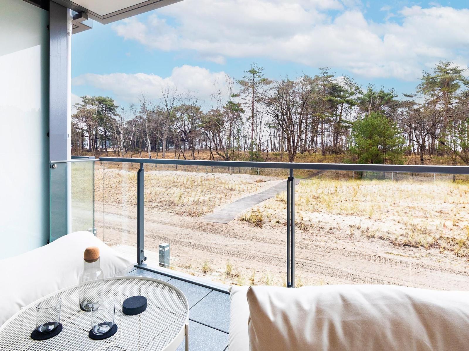 Terrasse mit Sitzgelegenheit und Blick auf Dünen und Wald.
