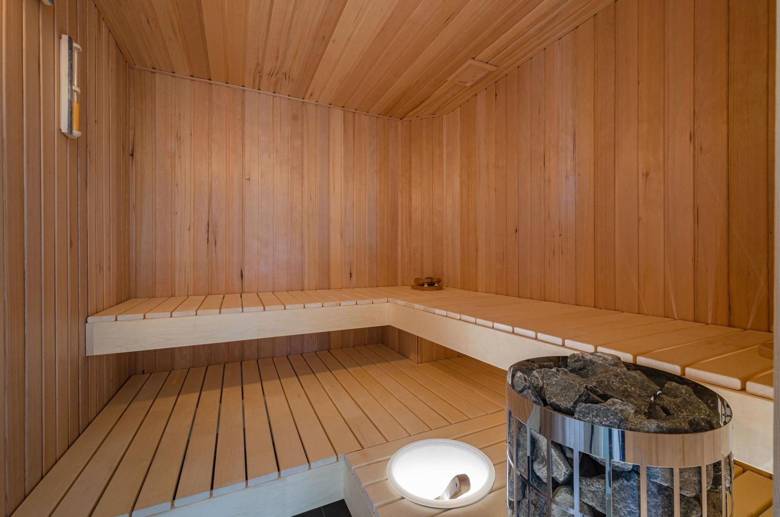 Sauna mit Holzwand, Sitzbänken und Steinkorb.