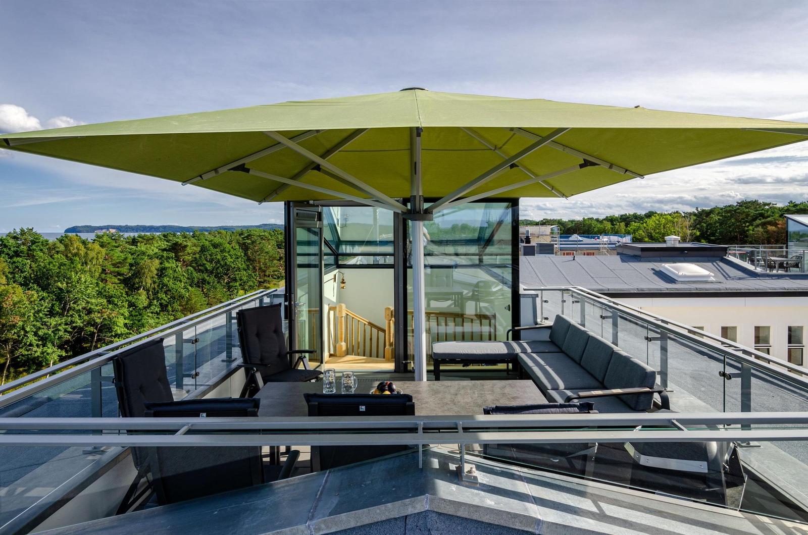 Terrasse mit Sitzgruppe, Sonnenschutz und Blick auf Wald und Wasser.