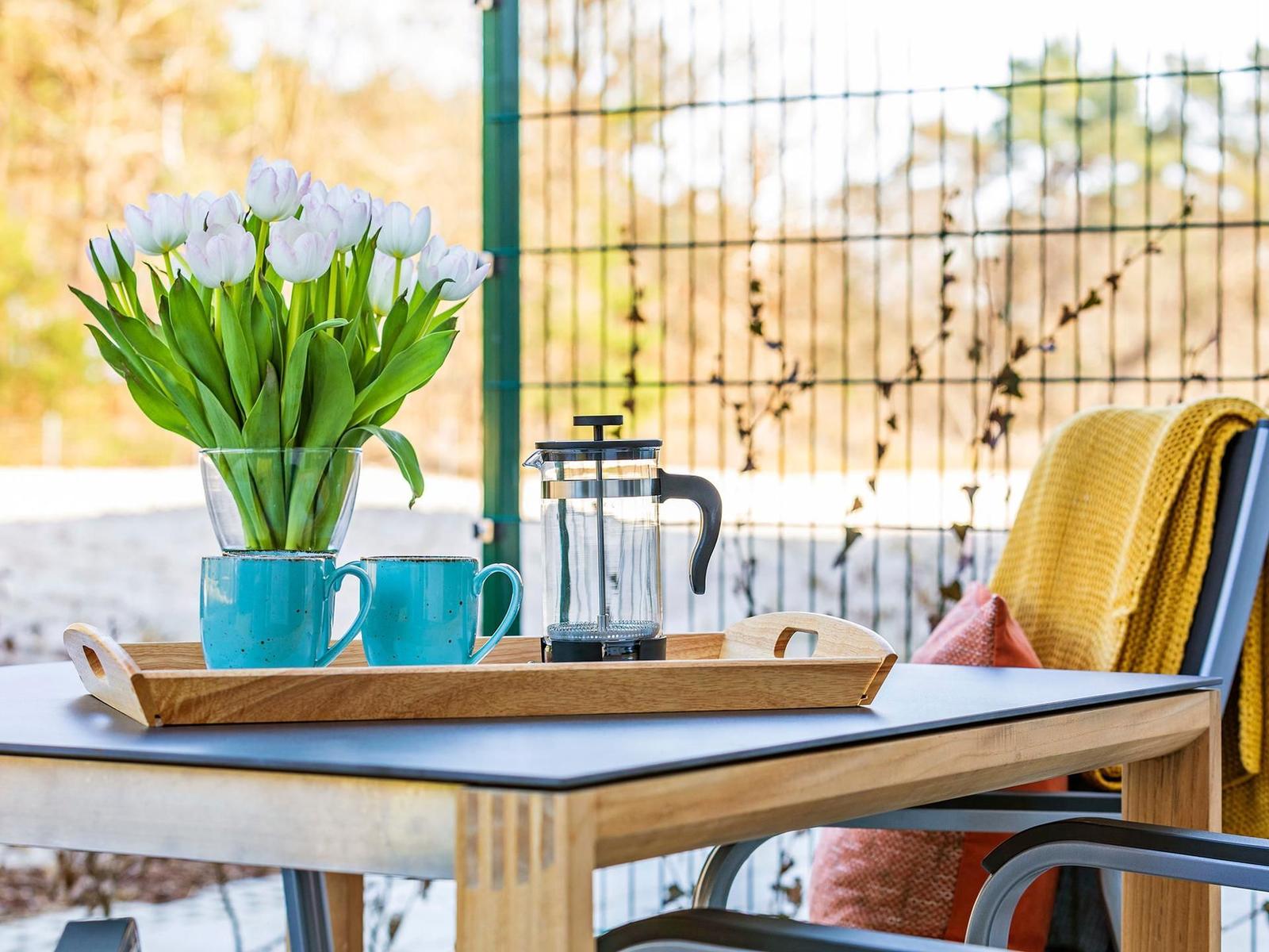 Auf der Terrasse steht ein Tisch mit einer Vase, zwei Tassen und einer Kaffeemaschine.