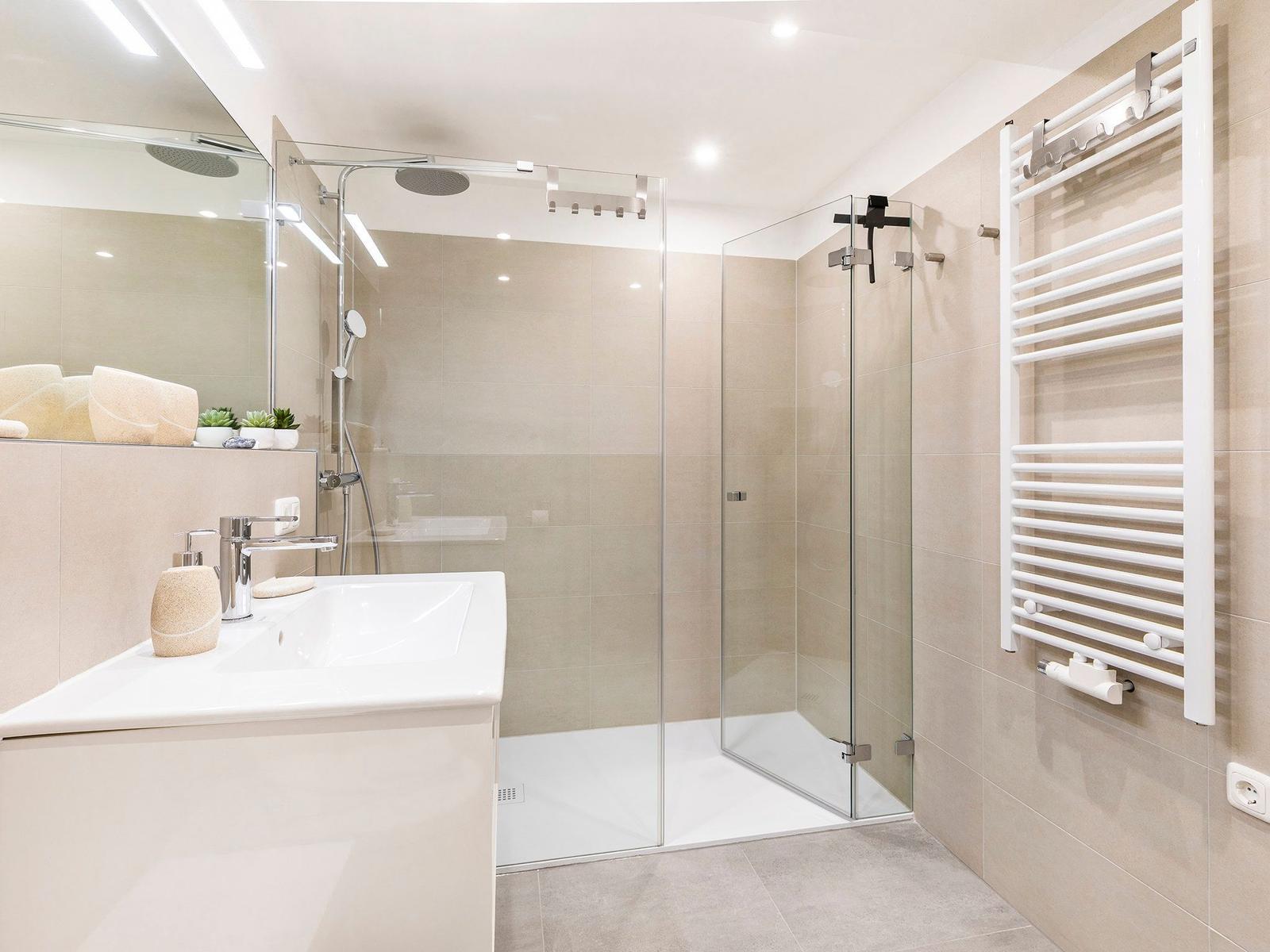 Moderne Dusche mit Glaswand, Waschbecken und Heizkörper an der Wand.
