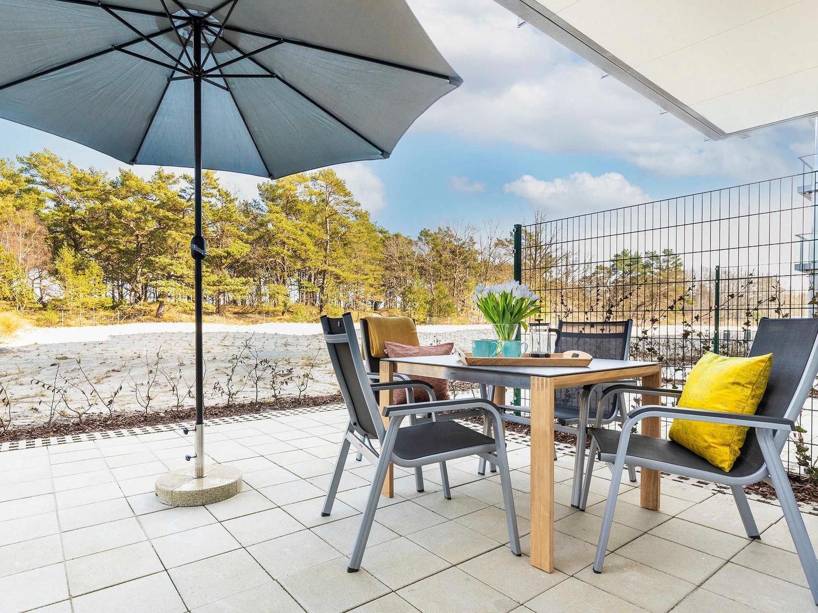 Terrasse mit Tisch, Stühlen, Sonnenschirm und Blick auf Wald.