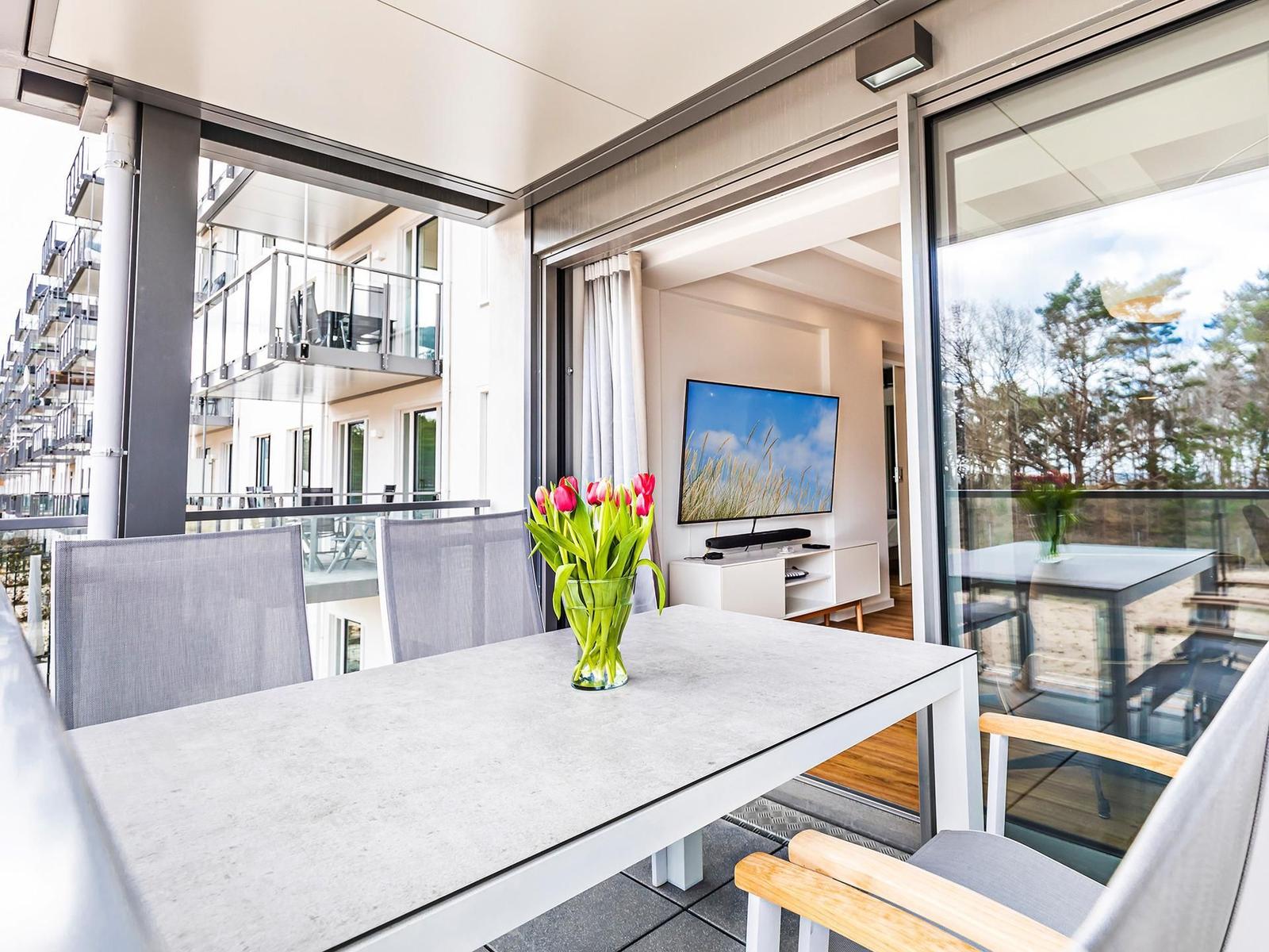 Terrasse mit Tisch und Stühlen. Im Hintergrund Wohnzimmer mit Fernseher.