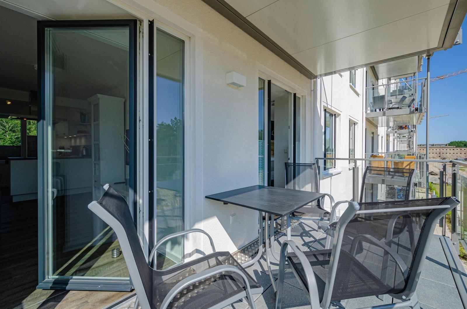 Terrasse mit Tisch und Stühlen, Glas-Türen zum Innenraum, Blick auf benachbarte Gebäude.