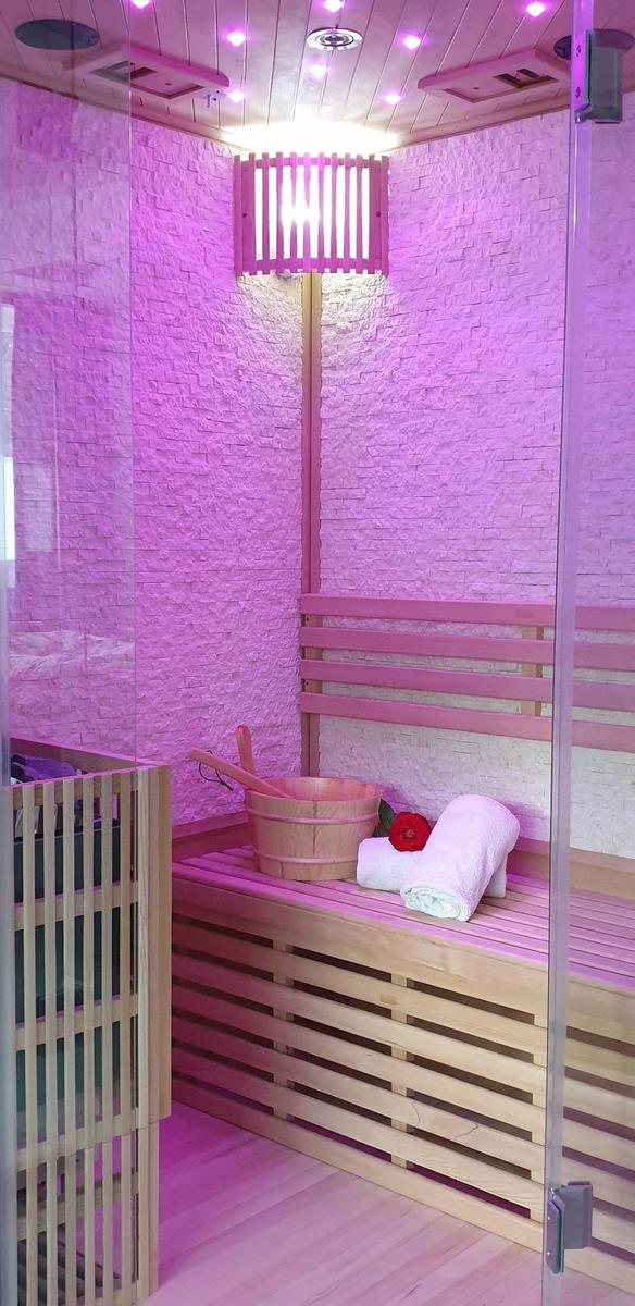 Sauna mit Holzbank, Eimer und Handtuch in pinker Beleuchtung.