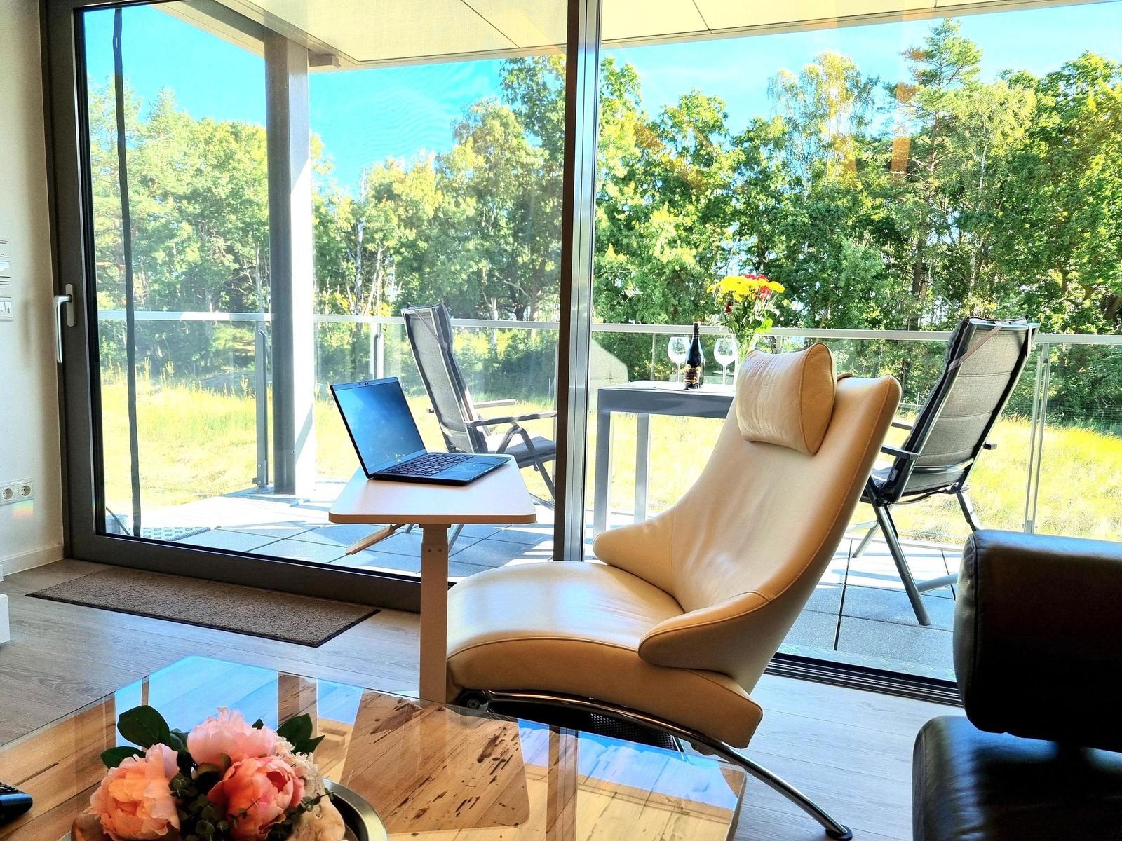 Bequeme Sitzgelegenheit mit Laptop und Blick auf Balkon mit Garten