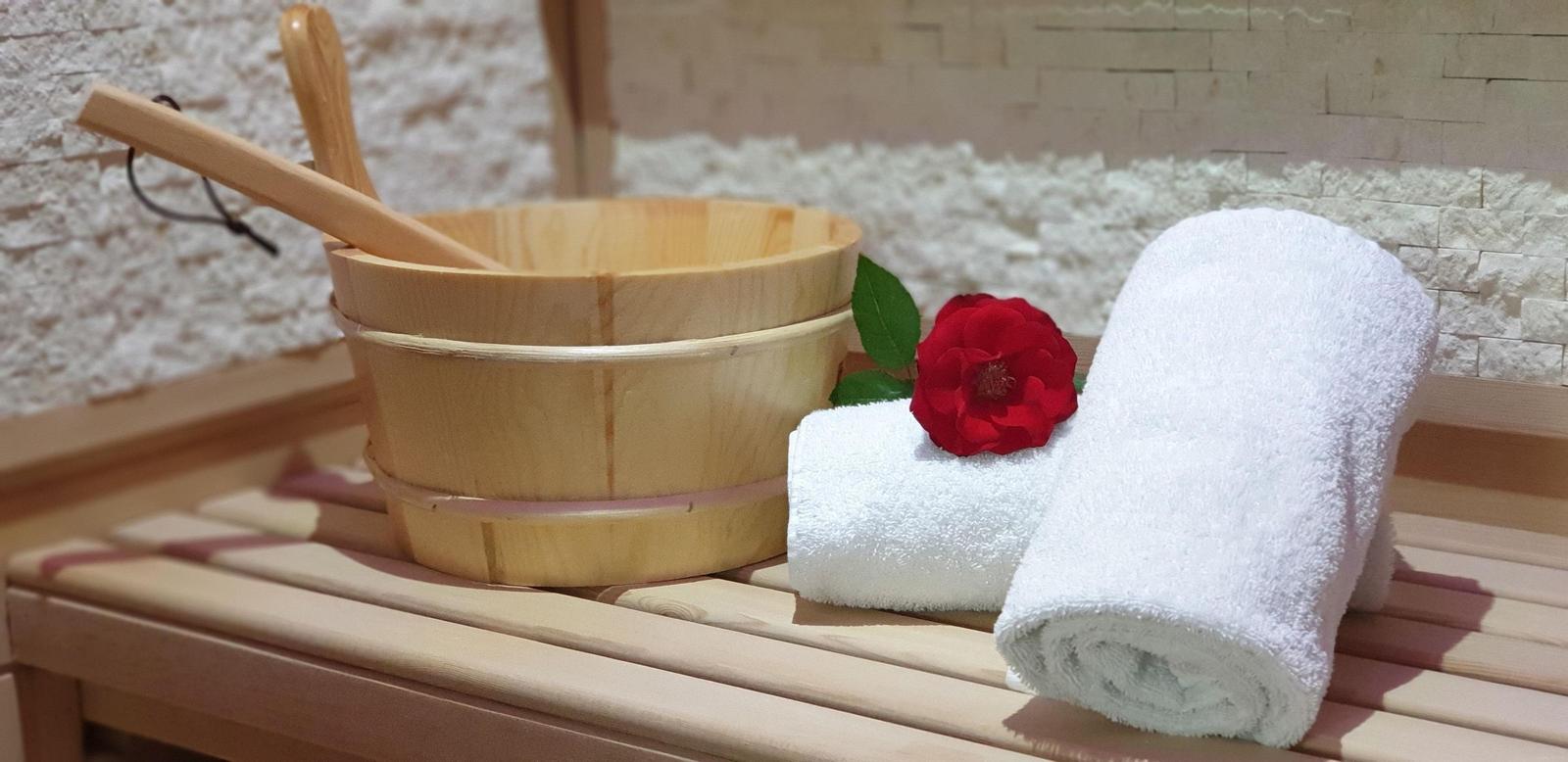 Holzbadewanne mit Handtuch und roter Rose auf Holzbank