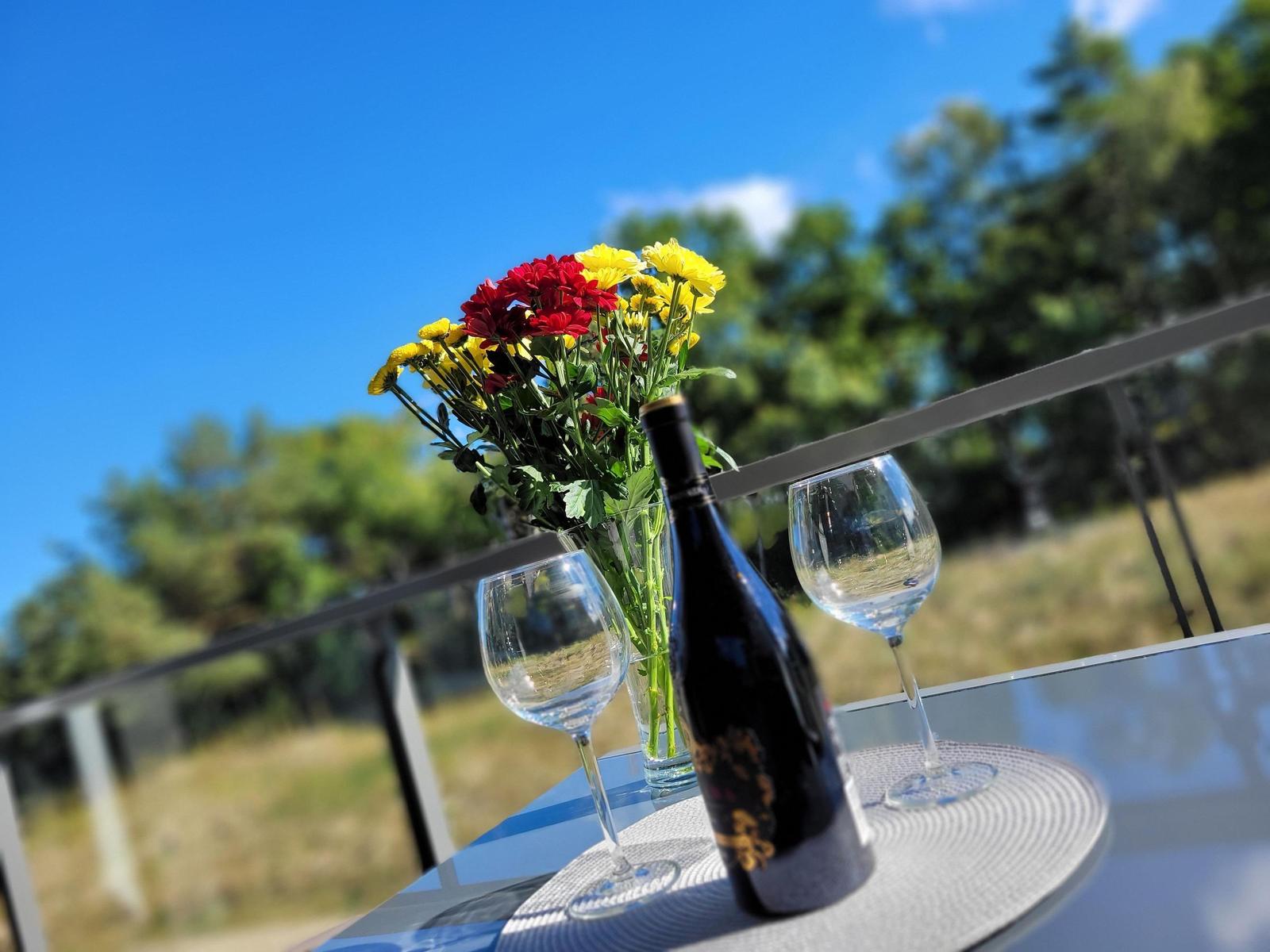 Auf der Terrasse steht ein Tisch mit einer Weinflasche, zwei Gläsern und einer Blumenvase.
