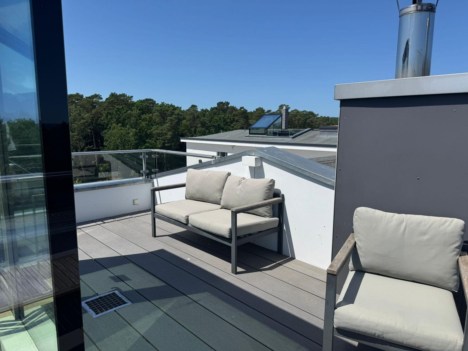 Terrasse mit Sitzgelegenheiten und Blick auf Wald und Gebäude