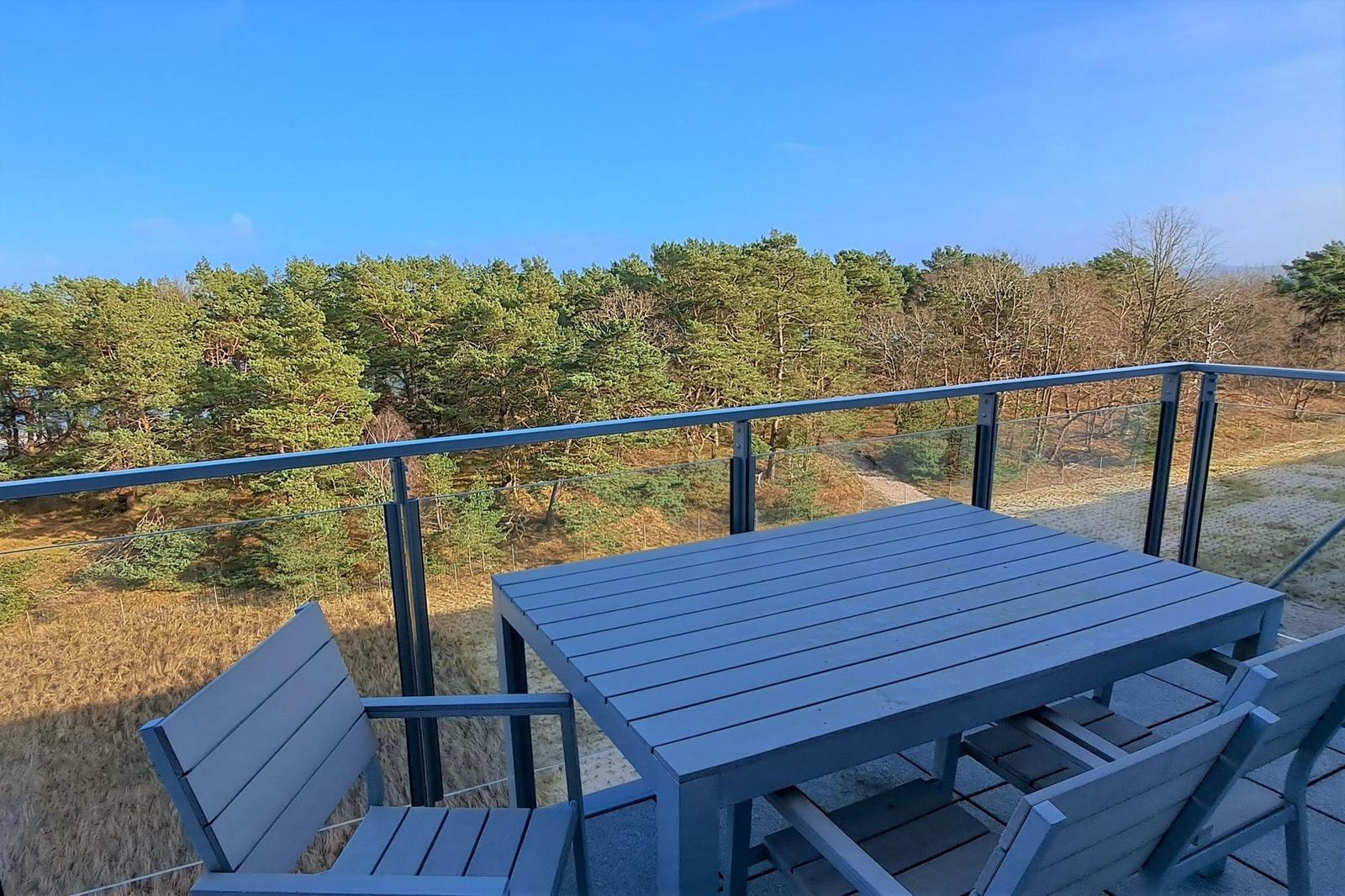 Terrasse mit Tisch und Stühlen. Blick auf Wald und Himmel.