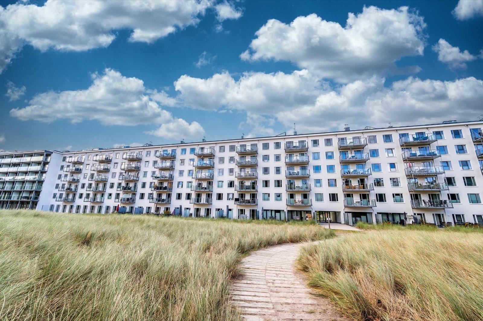 Apartment building with balconies and path through grassland under blue sky.