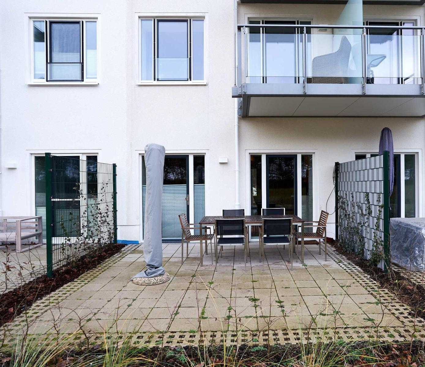Hinterhof mit Tisch, Stühlen und Balkon. Gartenbereich mit Pflanzen und Zaun.