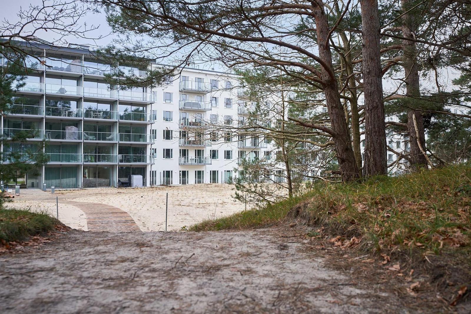Modernes Mehrfamilienhaus mit Balkonen und Sandstrand im Hintergrund.