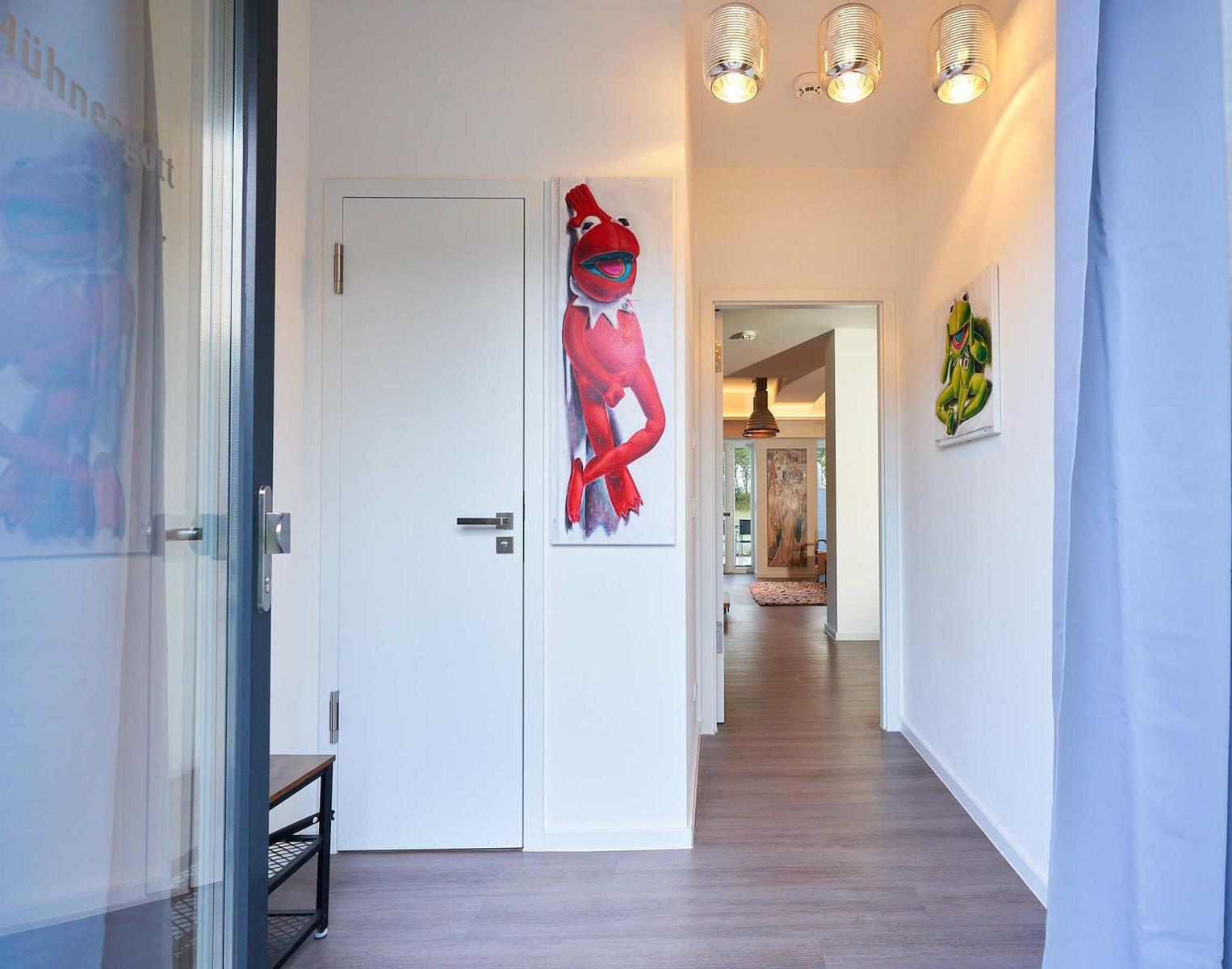 Flur mit Holzboden, weißen Wänden und Kunstwerken an den Wänden.