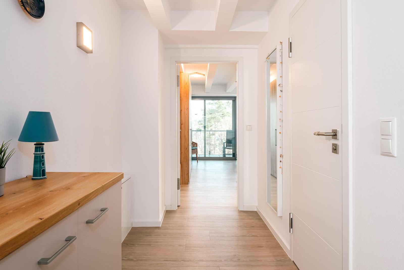 Flur mit Holzboden, Schrank und Blick in Wohnbereich mit Balkon.