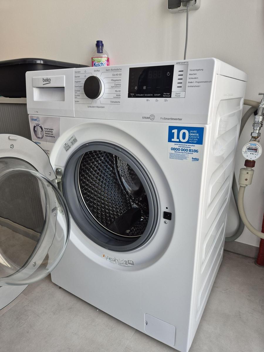 Weiße Frontlader-Waschmaschine mit geöffneter Tür und Bedienfeld.