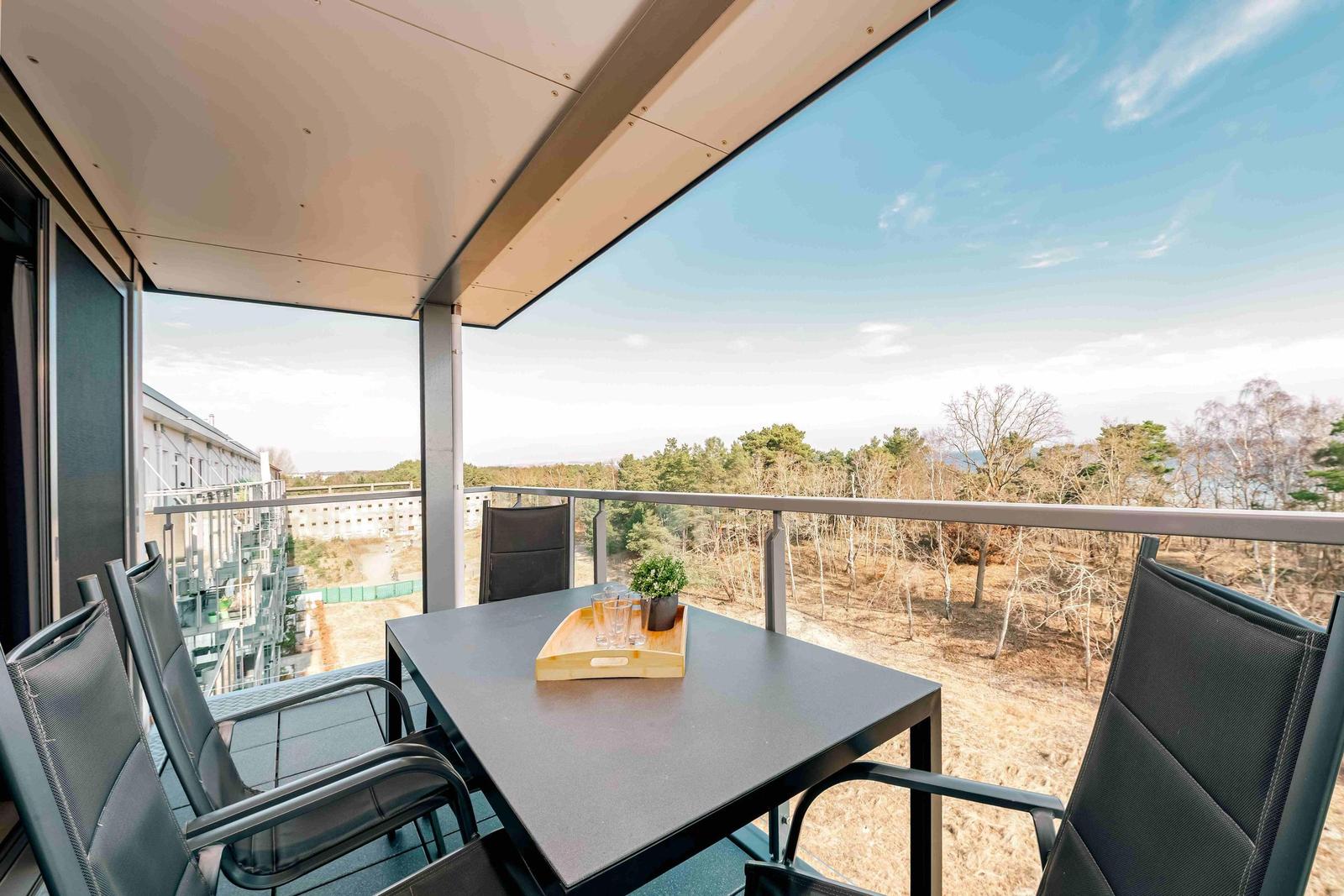 Terrasse mit Tisch und Stühlen. Blick auf Wald und Gebäude.