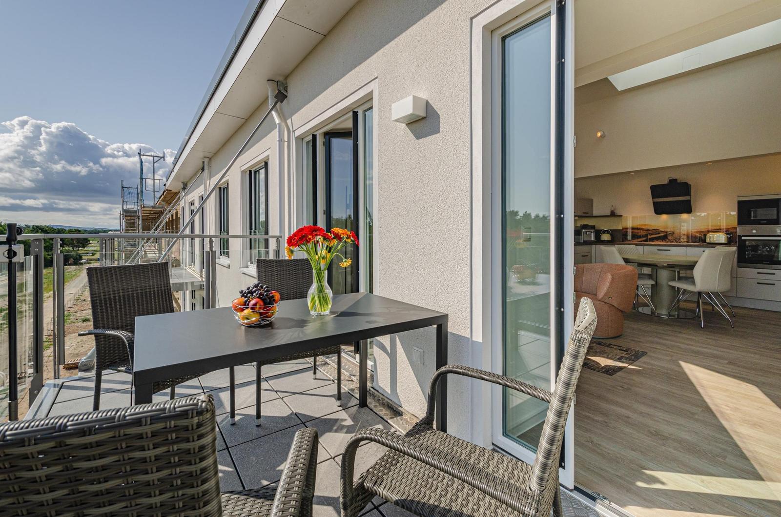 Terrace with table, chairs, and flowers. View into interior showing kitchen and living area.