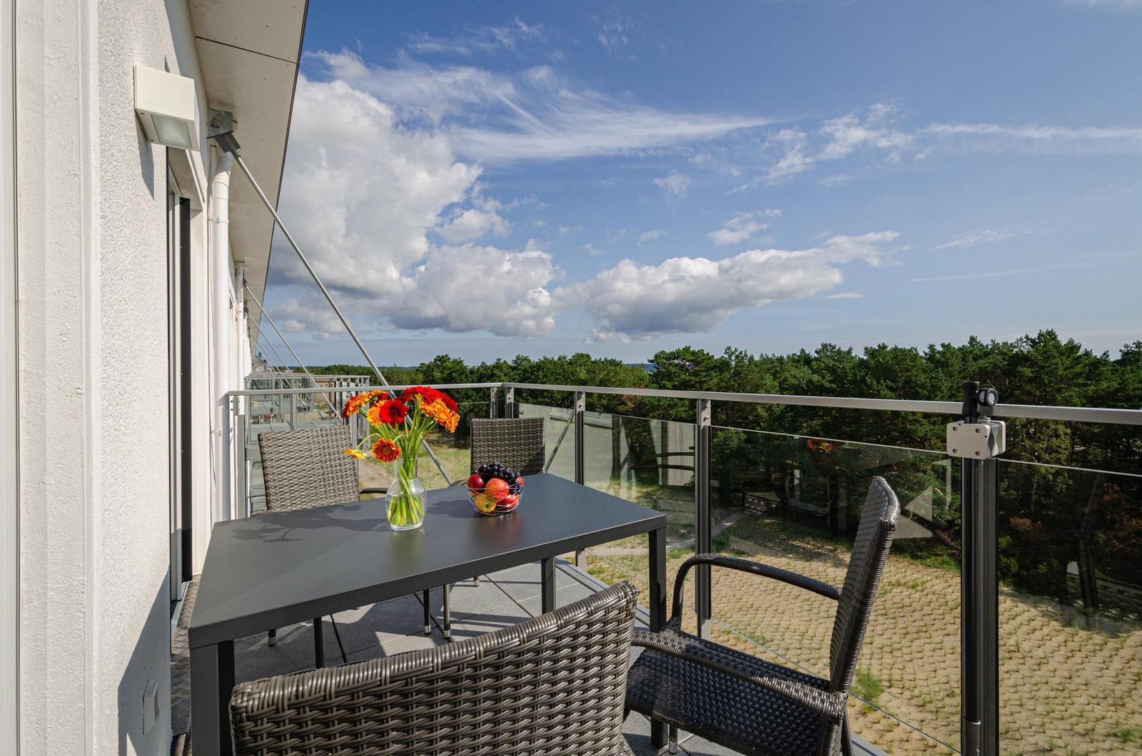 Terrace with table, chairs, flowers, and fruit. View of forest and sky.