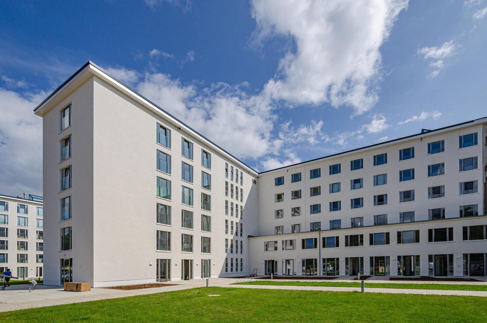 Modern multi-family building with white facade and green lawn area under blue sky.
