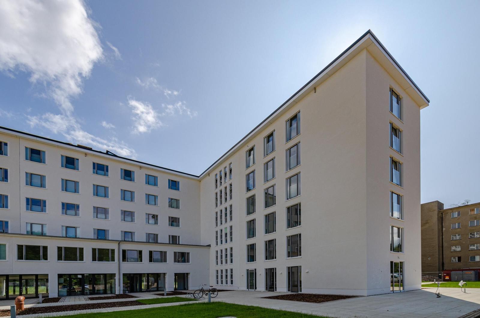 Modern residential building with multiple floors and glass windows under blue sky.