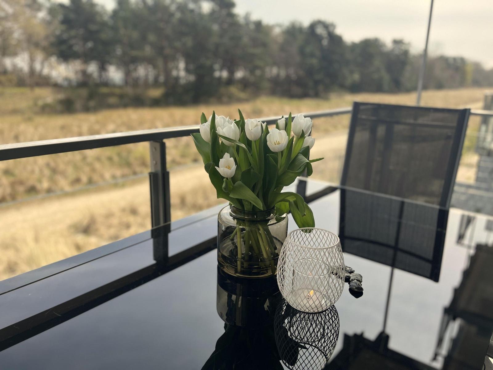Auf der Terrasse steht eine Vase mit weißen Tulpen und eine Teelichtlaterne.