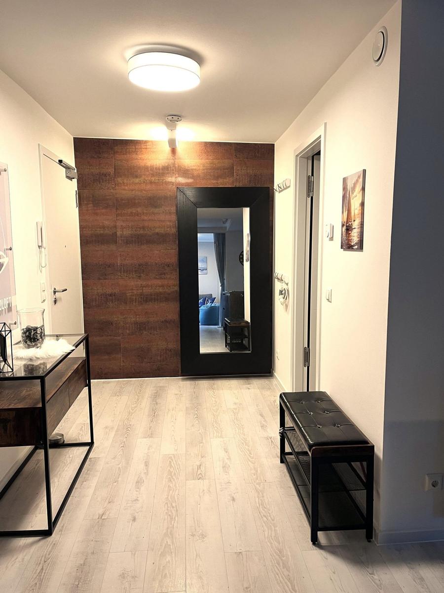 Eingangsbereich mit Holzboden, Spiegel und Bank. Wandverkleidung und moderne Beleuchtung.