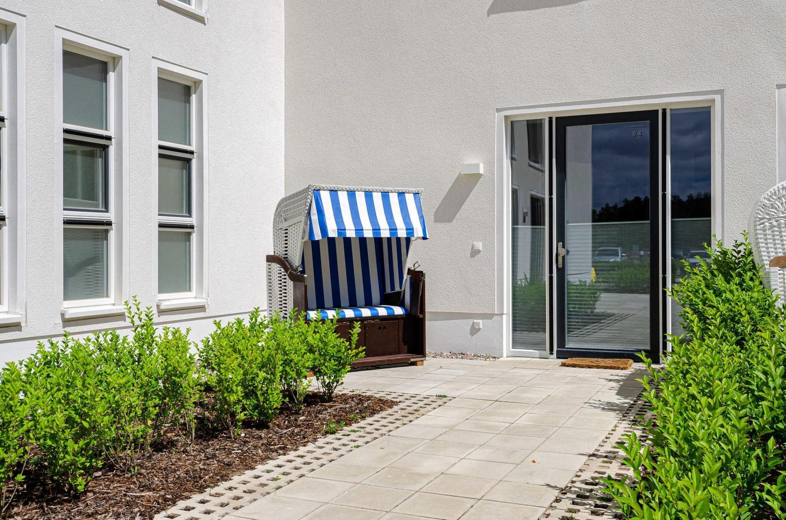 House with terrace, blue-and-white beach chair, and shrub beds.
