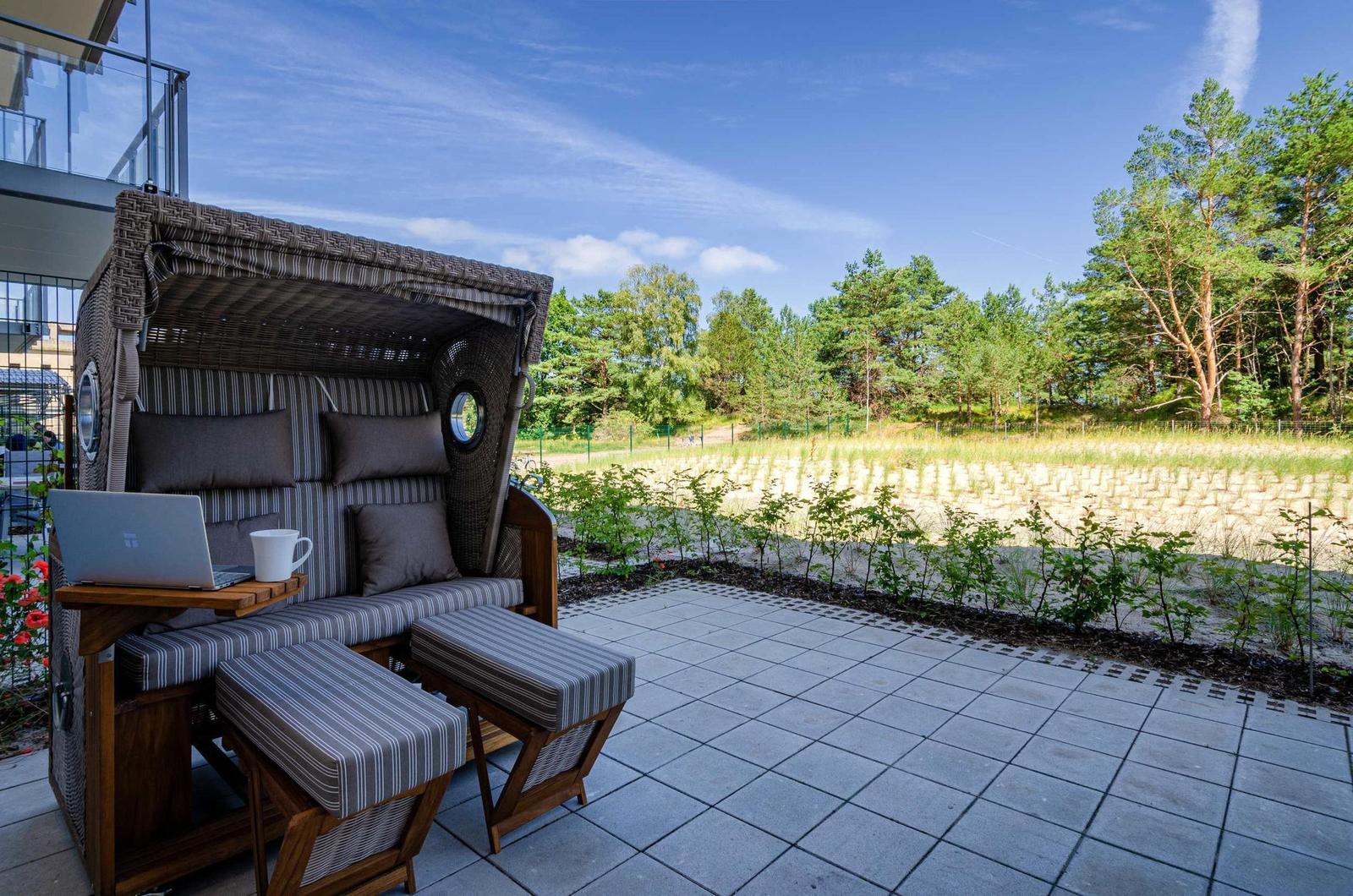 Terrace with beach chair, laptop, and cup. View of meadow and forest.