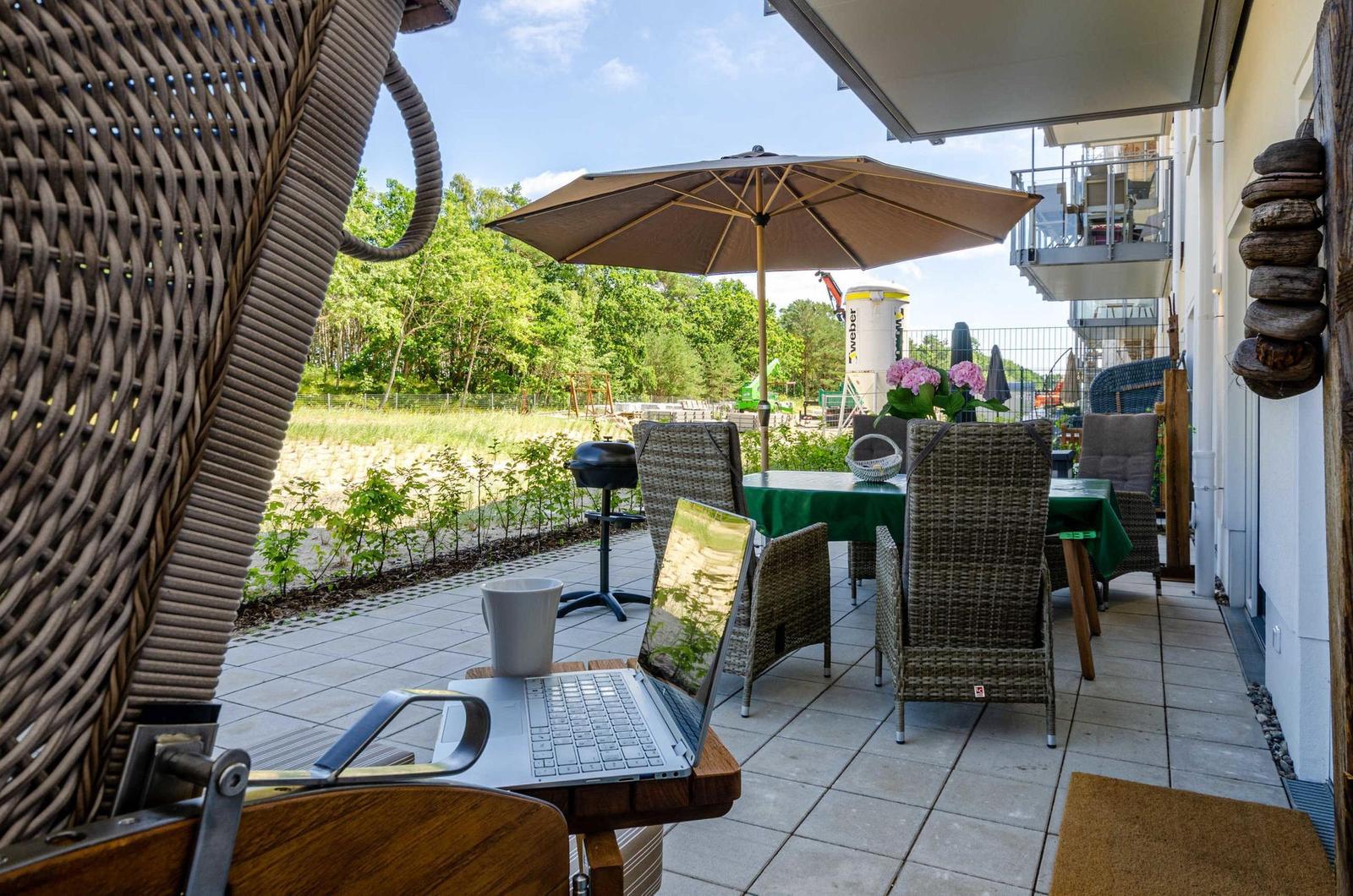 Terrace with table, chairs, and umbrella. Laptop and cup on a table.
