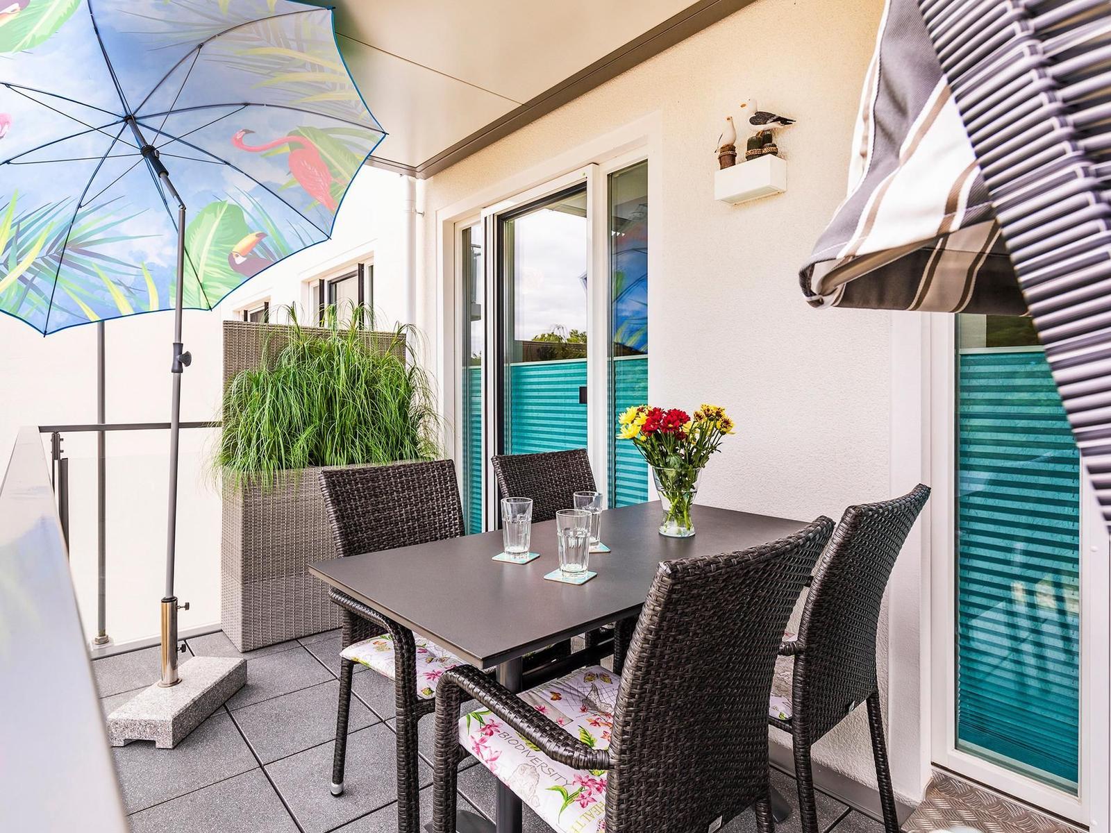 Terrasse mit Tisch, Stühlen, Sonnenschirm und Blumenarrangement.
