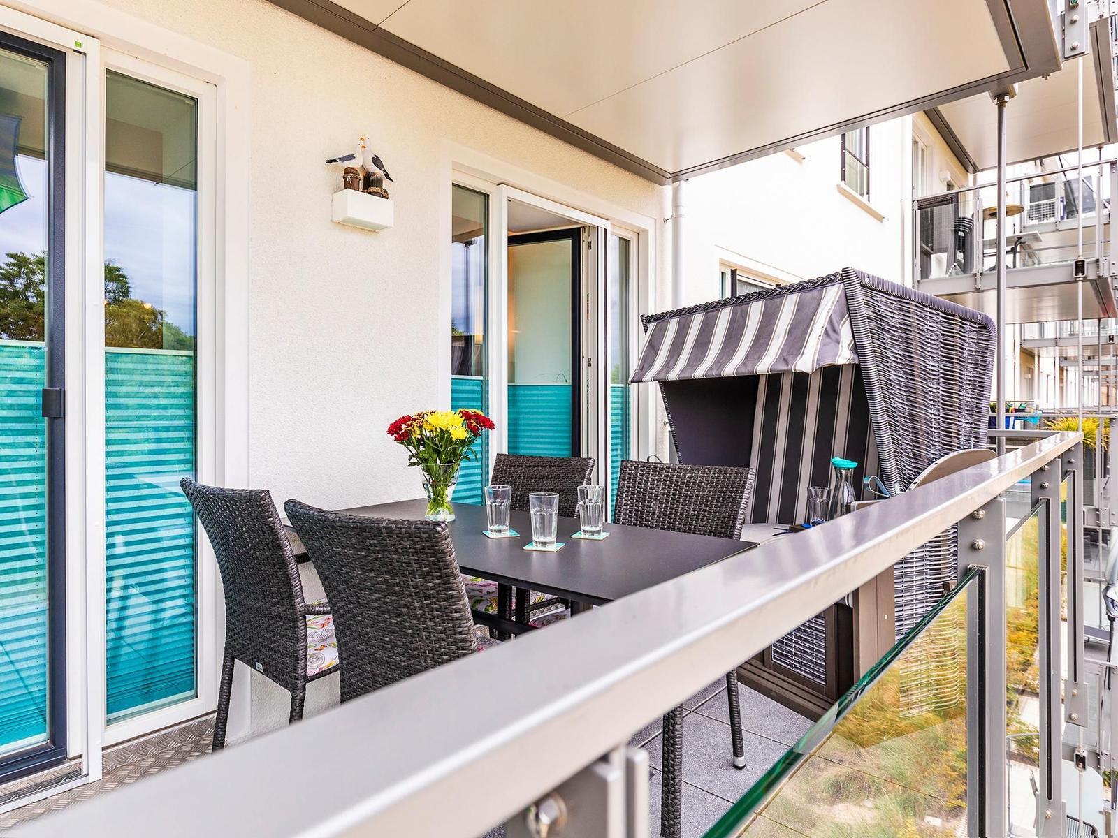 Terrasse mit Tisch, Stühlen und Sonnenschutz. Glasgeländer und Schiebetüren zum Innenraum.