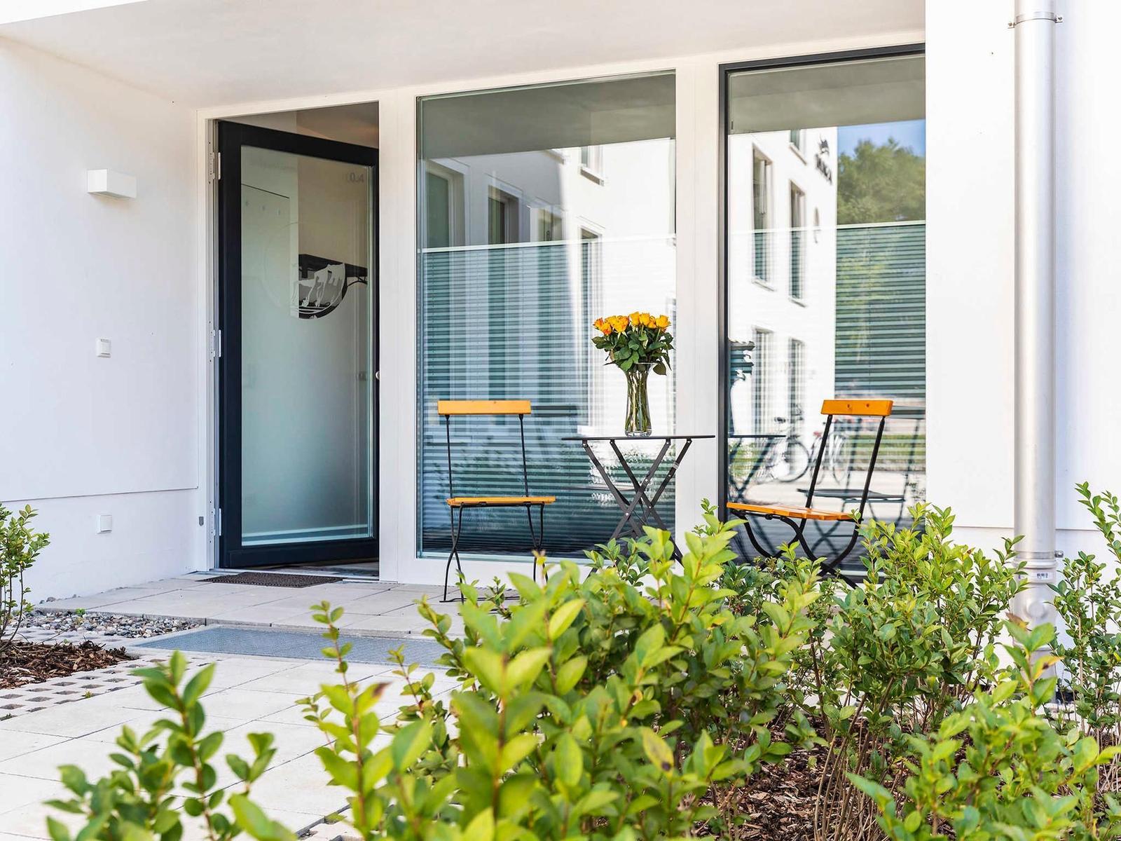 Eingangsbereich mit Glastür und kleinem Balkon mit Tisch und zwei Stühlen.