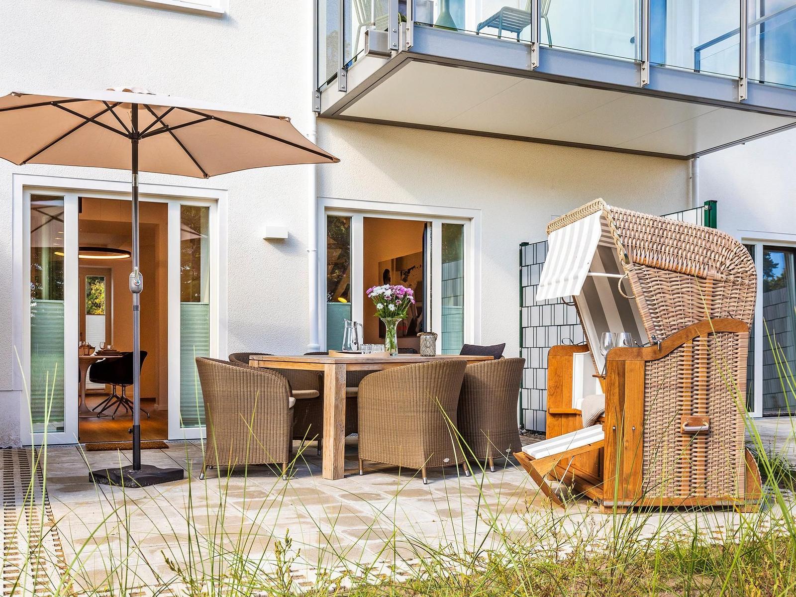 Terrasse mit Tisch, Stühlen, Sonnenschirm und Strandkorb. Durchgang in das Haus.