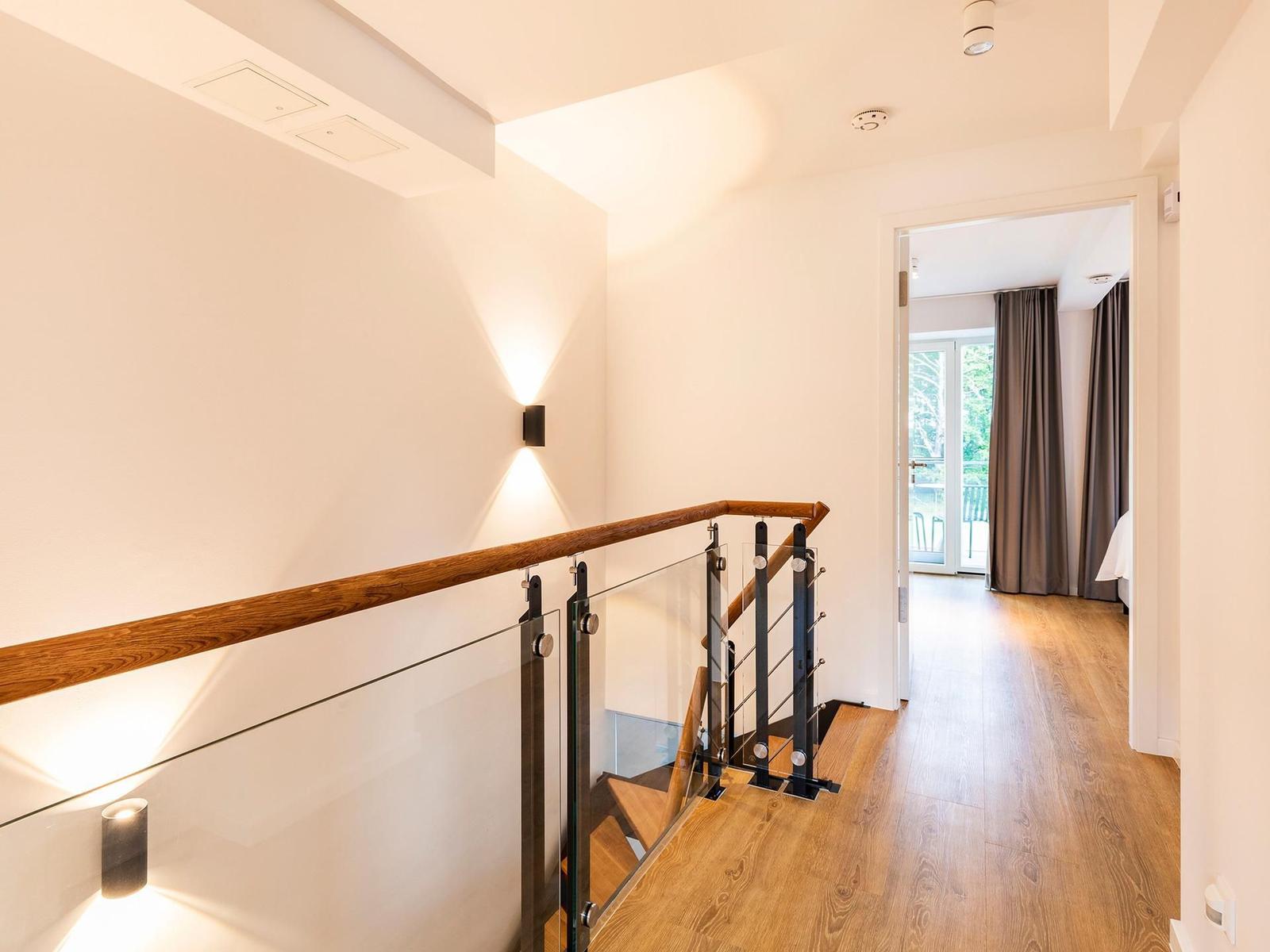 Haus mit Holztreppenhaus und Glasgeländer. Durchgang zur Schlafzimmer mit Blick auf Balkon.