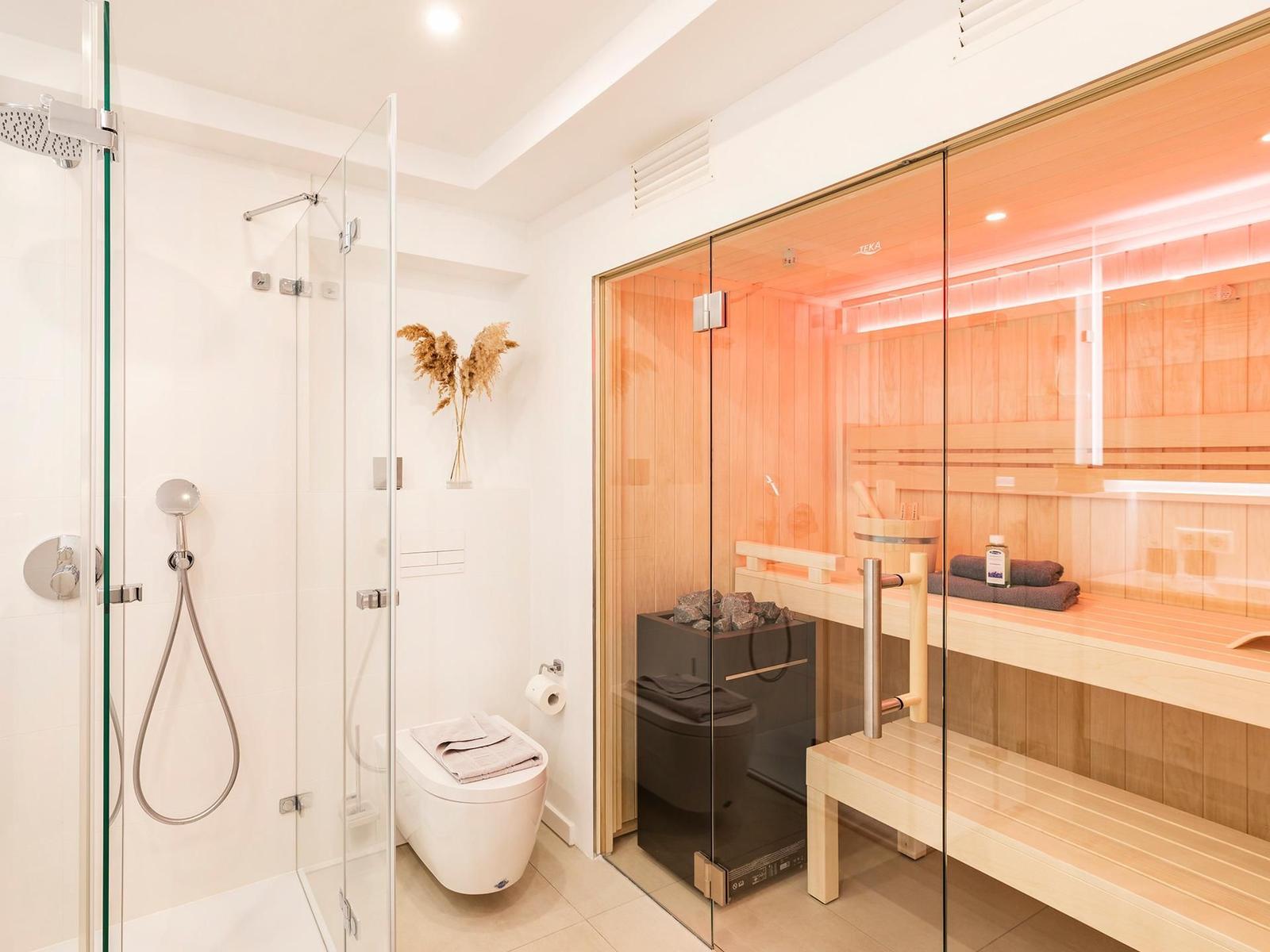 Dusche mit Duschbrause, Toilette und Sauna mit Holzbank und Steinen.