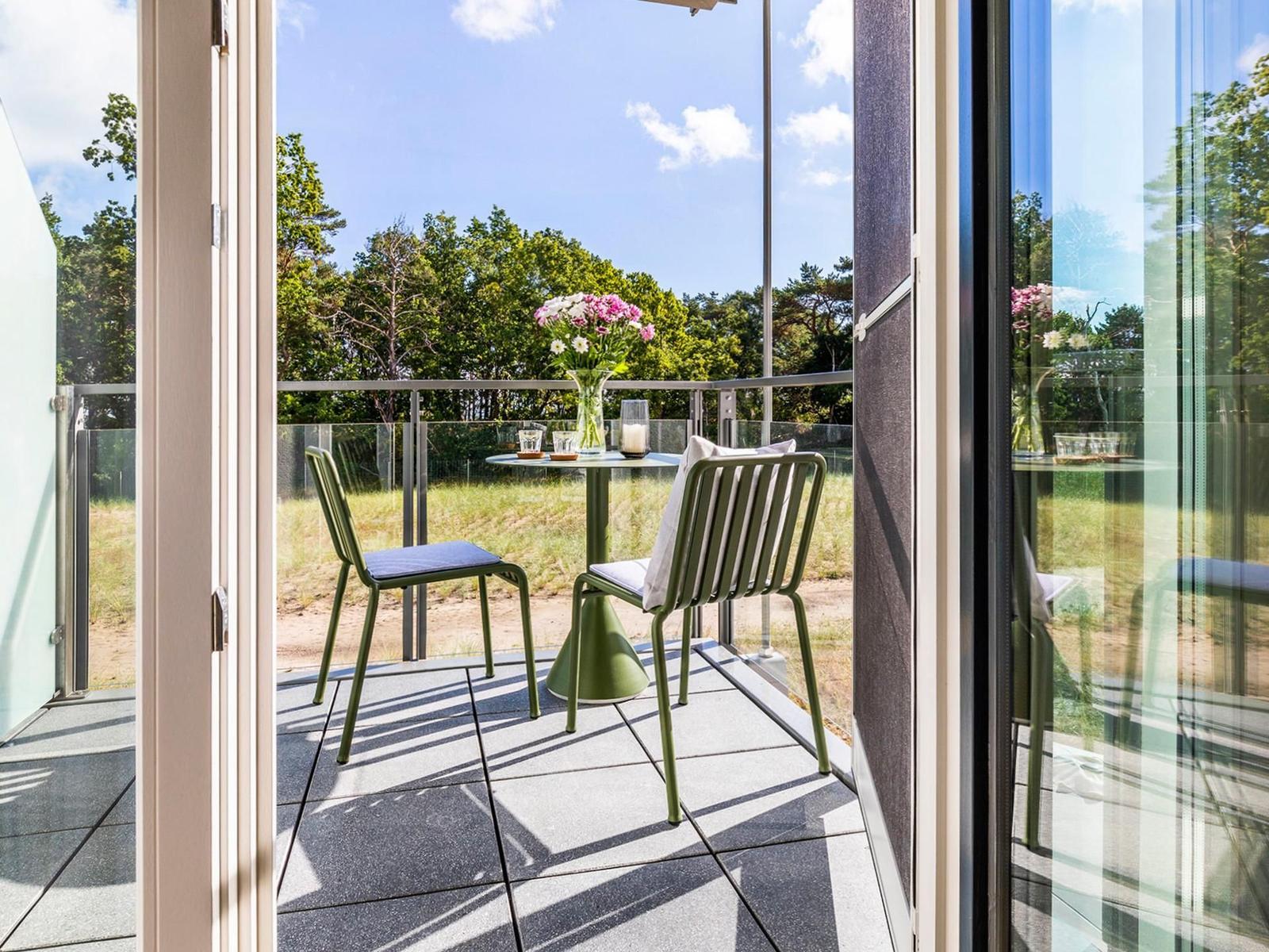 Terrasse mit Tisch und zwei Stühlen, Blick auf Wald und Himmel.