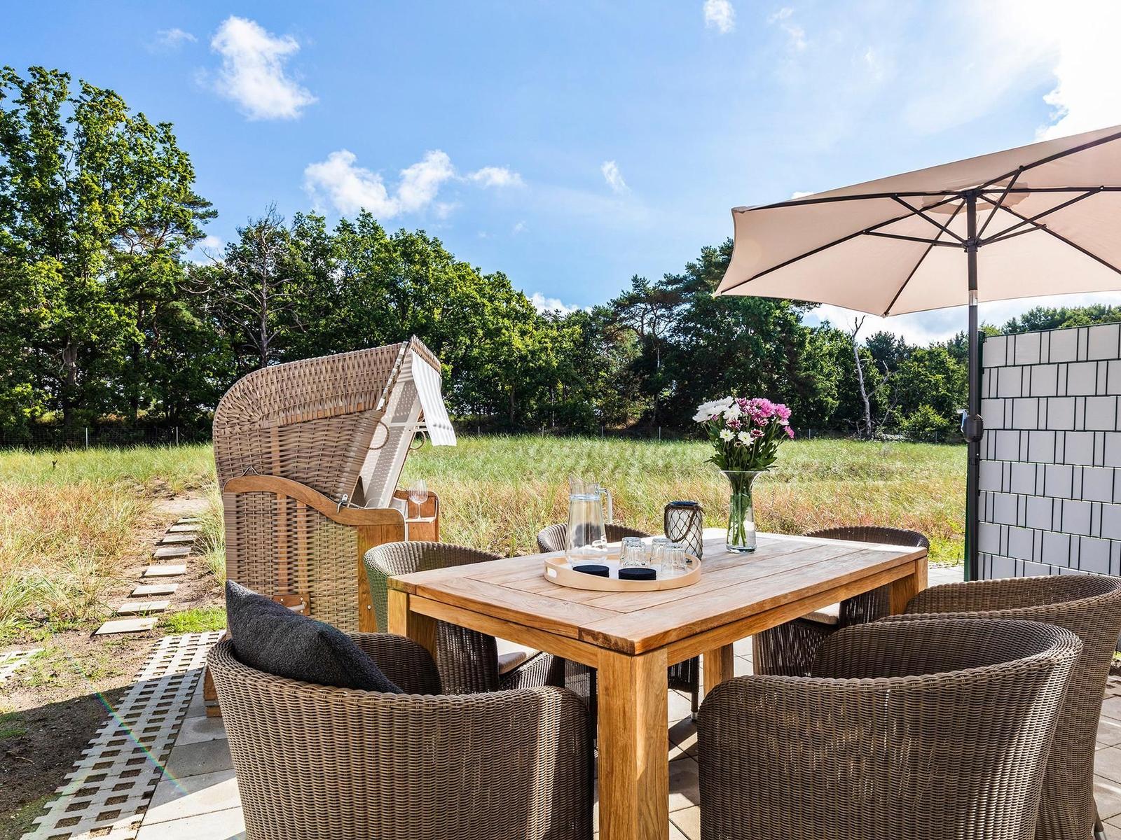 Terrasse mit Holztisch, Stühlen, Sonnenschirm und Liegestuhl vor Grünfläche.